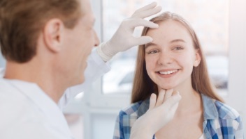 Young female getting face examined by male doctor)